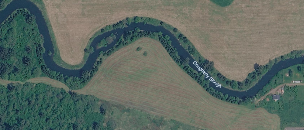 Aerial view of a winding stream labeled “Dougherty Slough” surrounded by fields and trees, with some buildings in the lower right corner.