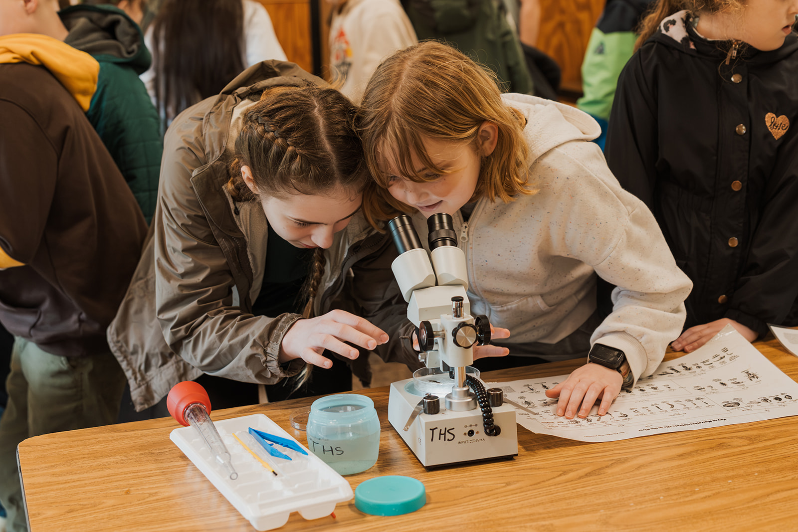 two grils looking into a microscope at a water sample